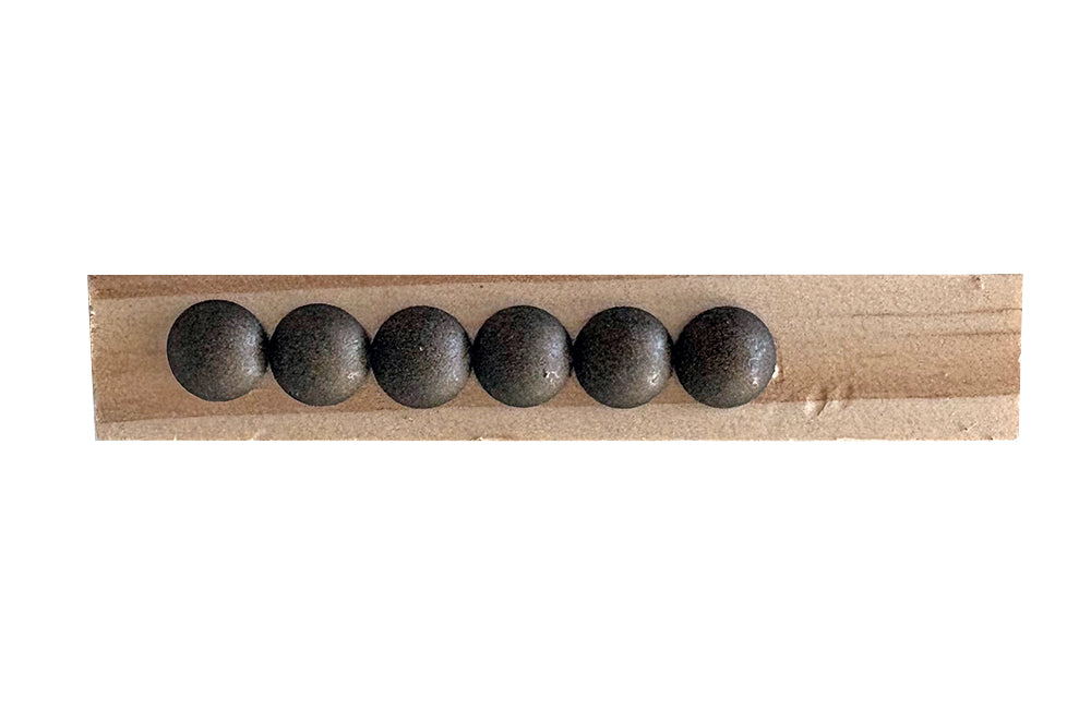 Five dark gray nailheads on a wooden stick against a white background